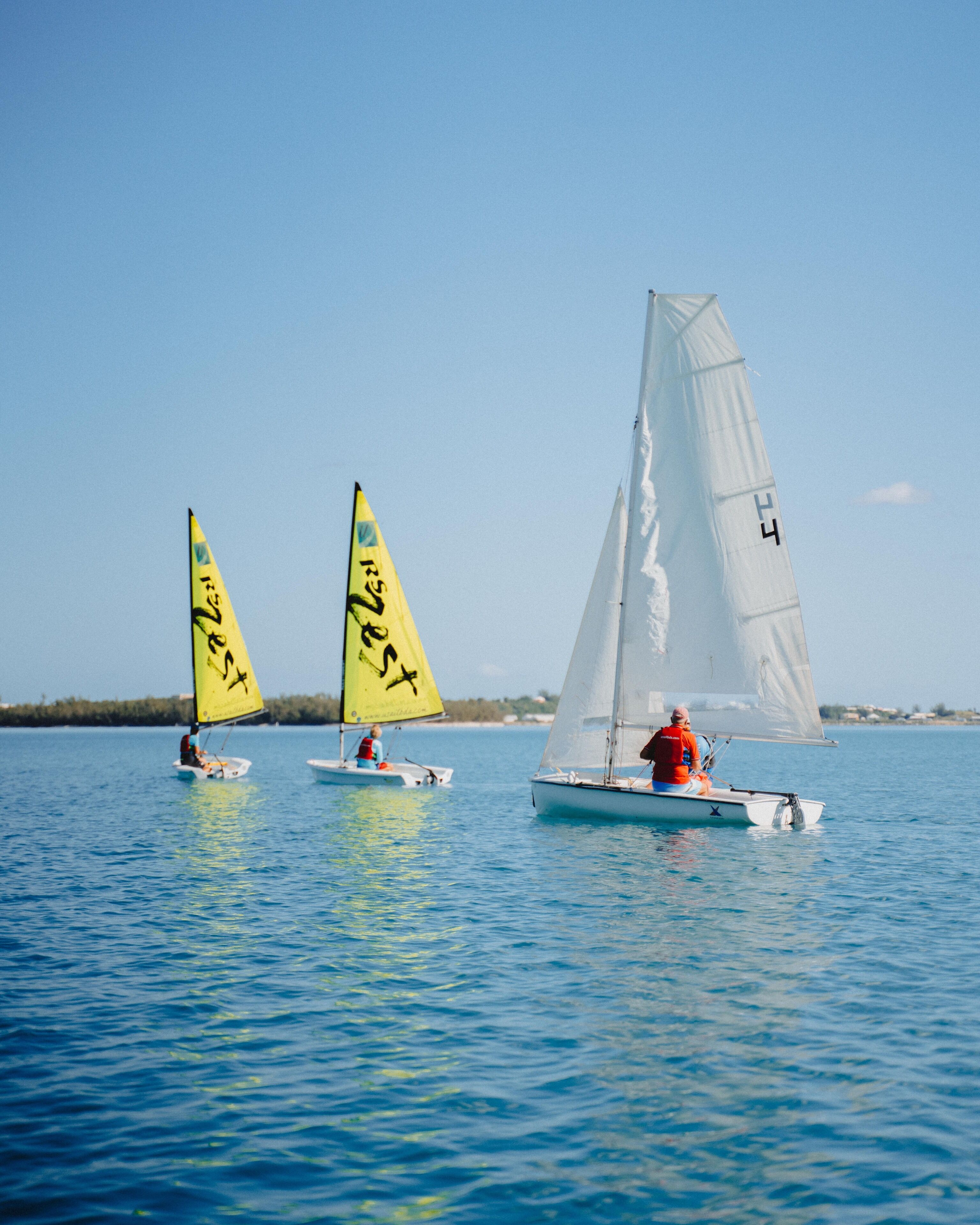 Three sailboats on calm water with clear skies.
