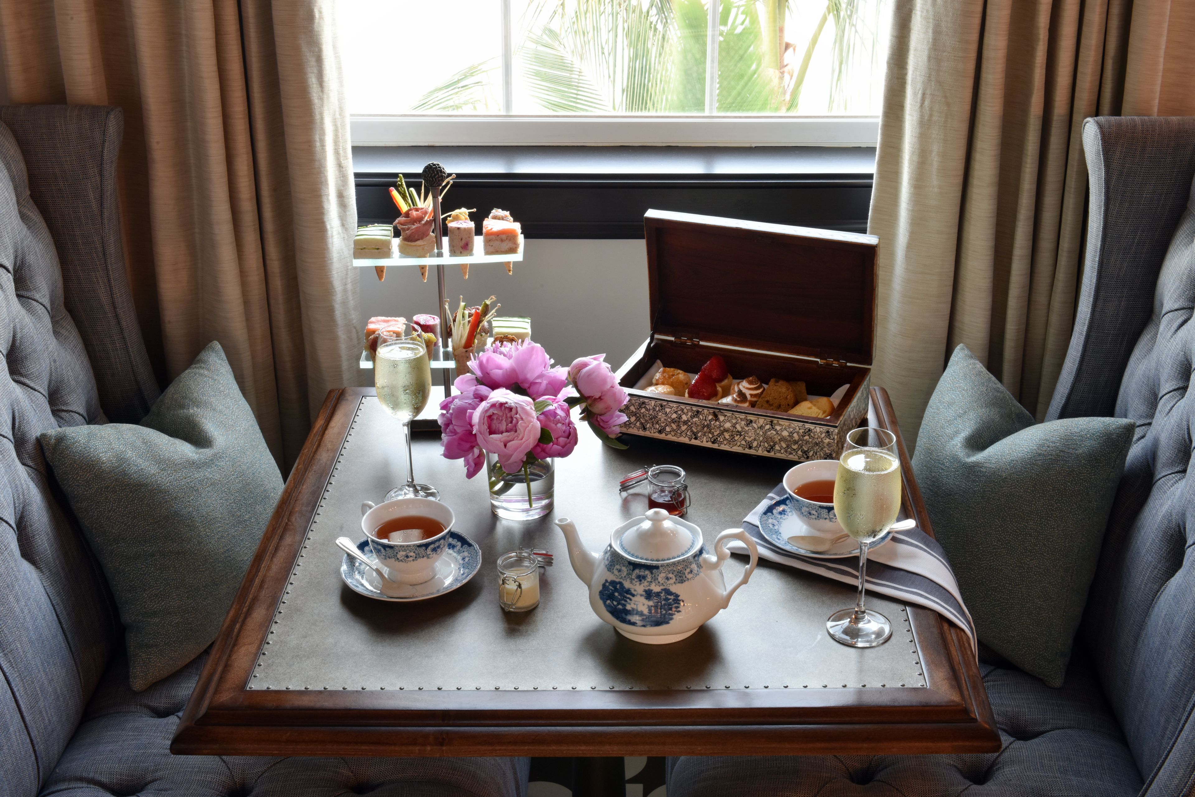 A table set with tea, a teapot, a tray of pastries, and a vase of flowers.