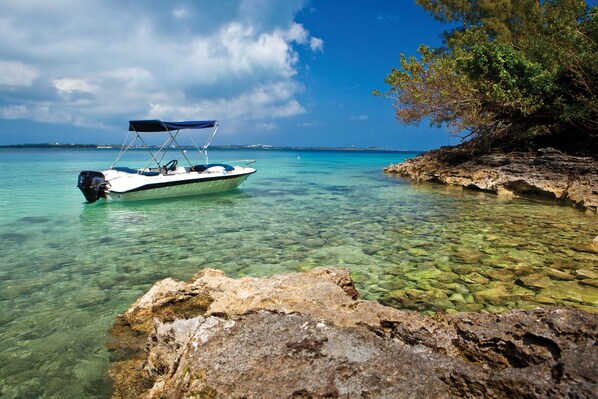 A boat anchored near clear waters with rocky shorelines and distant land. - Rosewood Bermuda (Hamilton Parish)