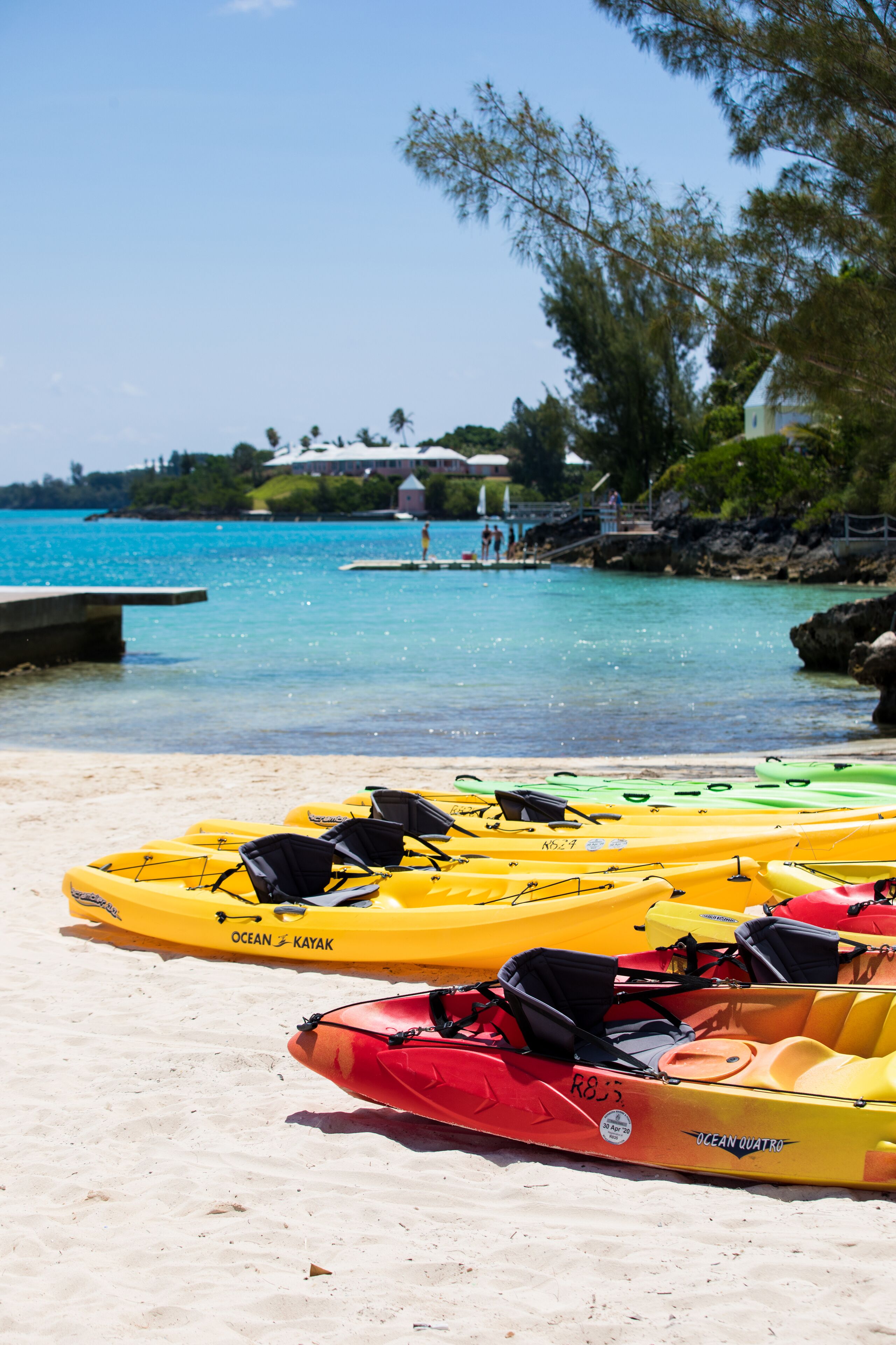 Una playa con kayaks alineados en la arena, un muelle y un cielo azul despejado.