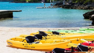 Una playa con kayaks alineados en la arena, un muelle y un cielo azul despejado.