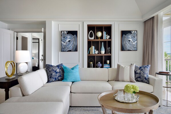 A modern living room with a sectional sofa, a coffee table, and a bookshelf with decorative items. - Rosewood Bermuda (Hamilton Parish)