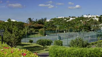 A tennis court surrounded by lush greenery and a clear blue sky.