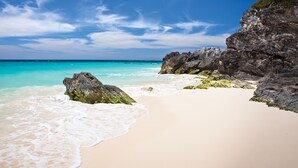 Una playa con agua turquesa cristalina, arena blanca y formaciones rocosas.