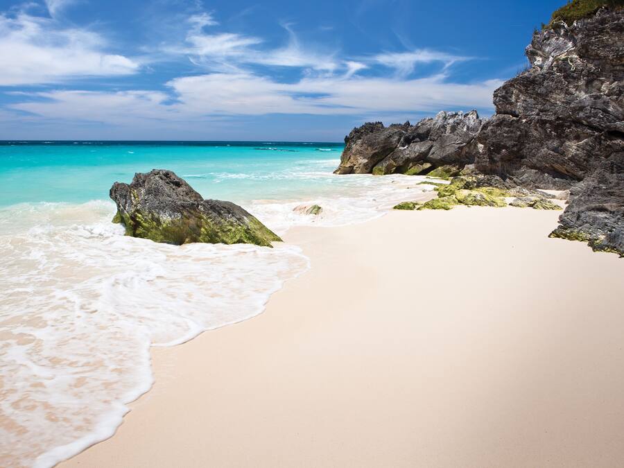 Una playa con agua turquesa cristalina, arena blanca y formaciones rocosas.