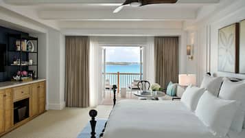 Een hotelkamer met een groot bed, een bureau met een computer, een boekenkast, een balkon met uitzicht op zee en een plafondventilator.