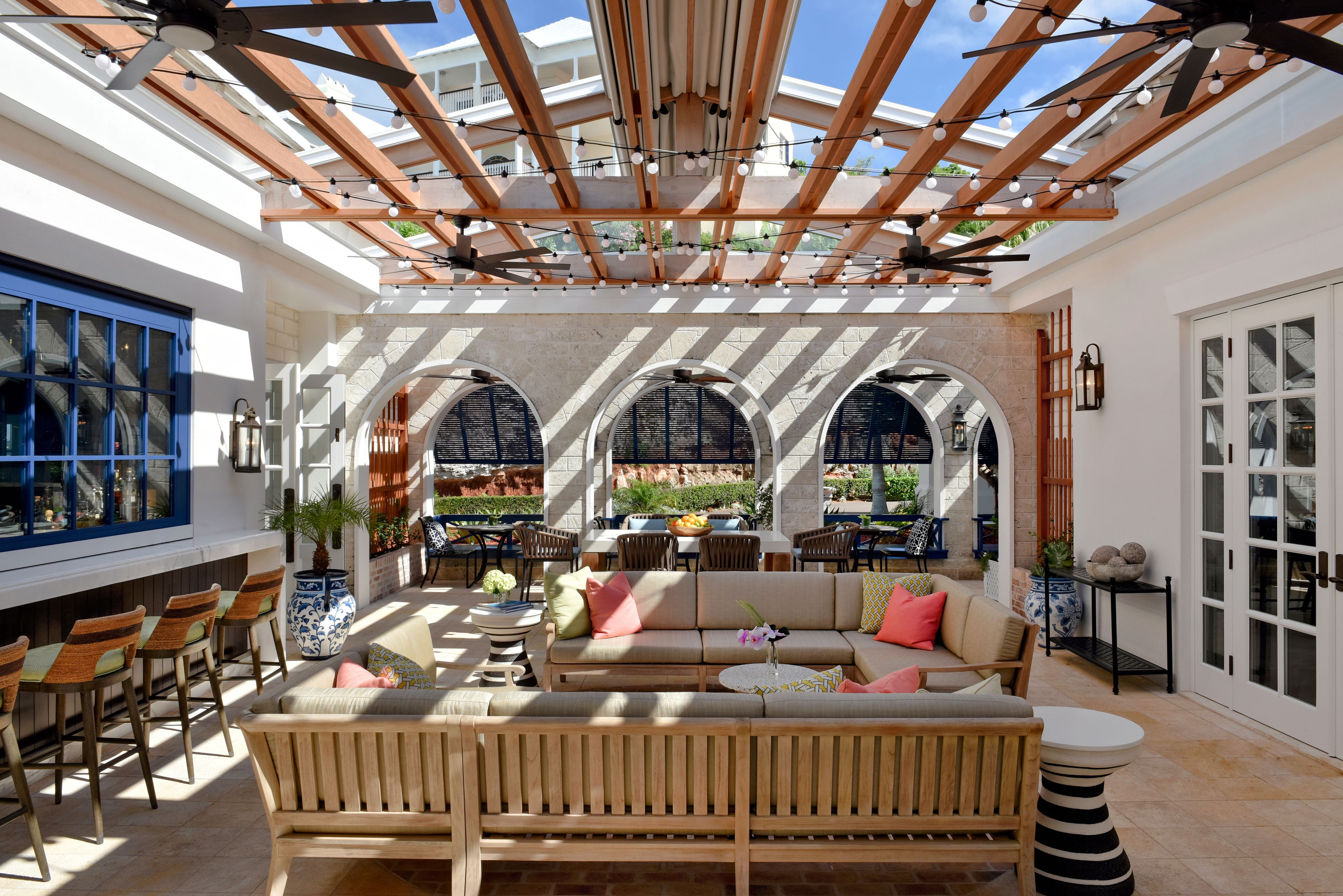 An outdoor patio area with a wooden pergola, seating arrangements, and a view of the garden.