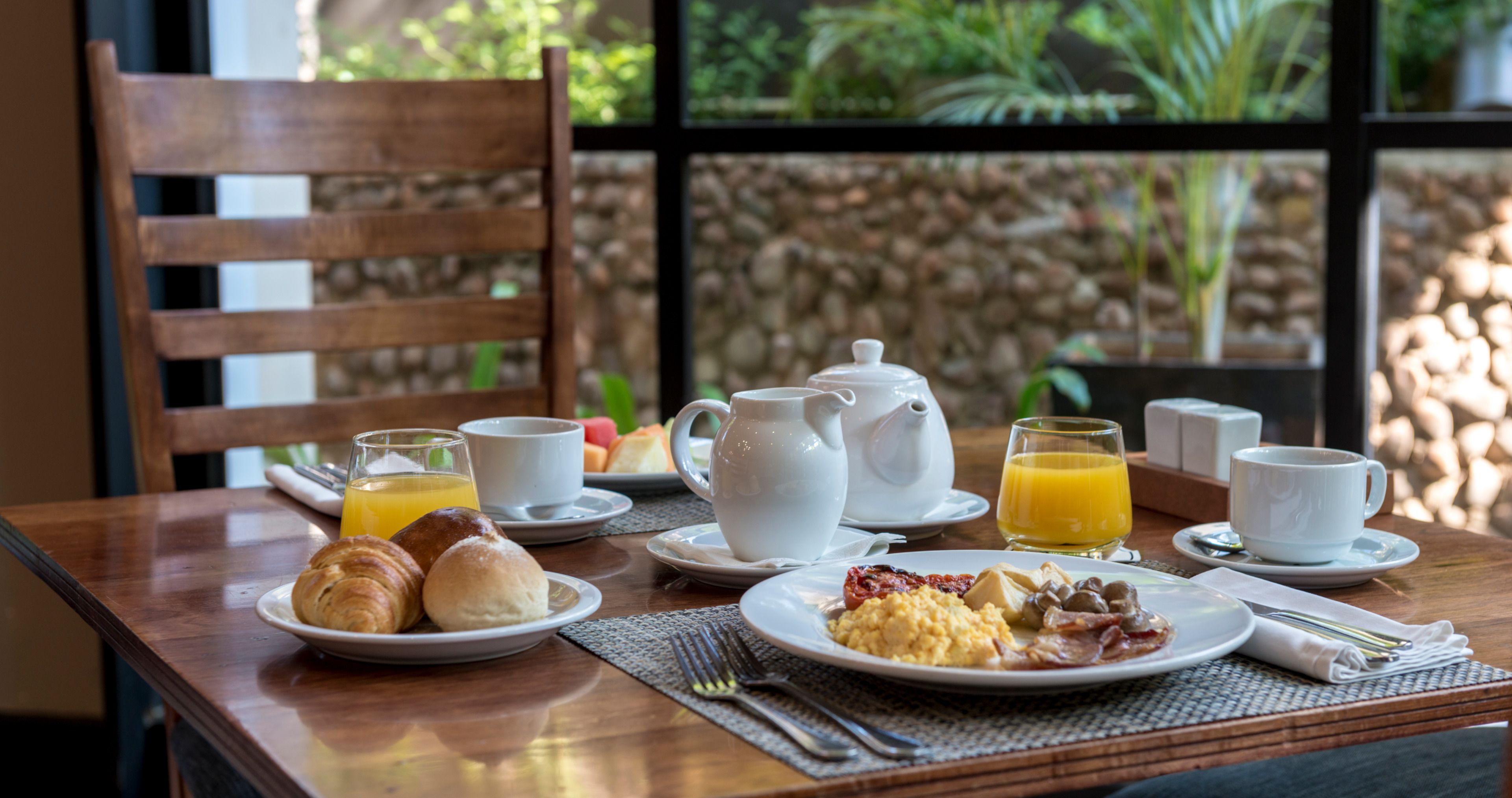 A breakfast table with croissants, scrambled eggs, bacon, and orange juice.