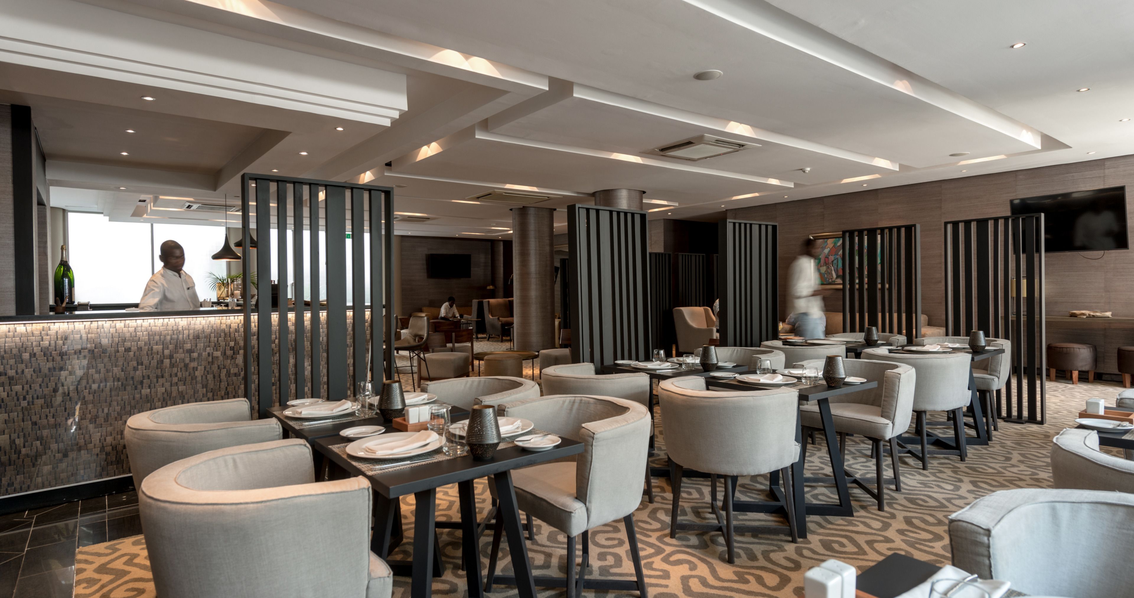 A modern restaurant with high tables and chairs, a bar area, and a TV screen.