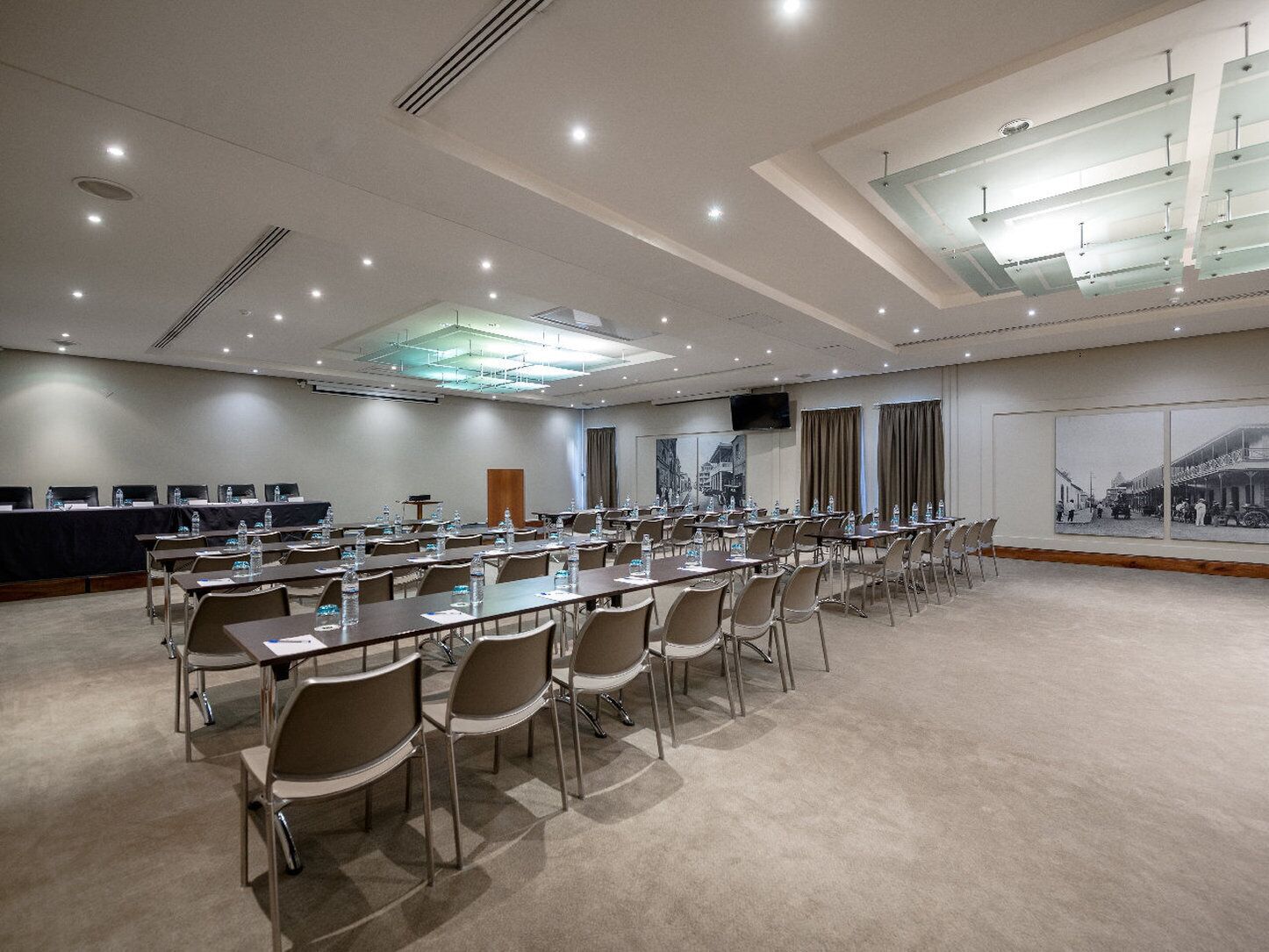 A conference room with long tables and chairs, a large window with curtains, and a mounted television on the wall.