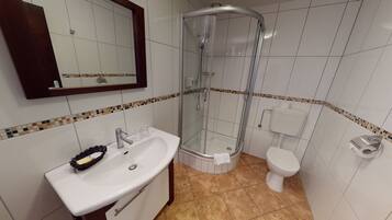 Un baño con cabina de ducha de vidrio, un lavabo blanco con jabonera y un inodoro.