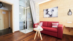 A modern room with a red sofa, a glass partition, a wooden floor, and a wooden wall with a painting. - Hotel San Marco (Lannach)