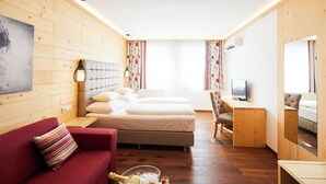 A hotel room with wooden walls, a bed, a red sofa, a TV, and a small desk. - Hotel San Marco (Lannach)