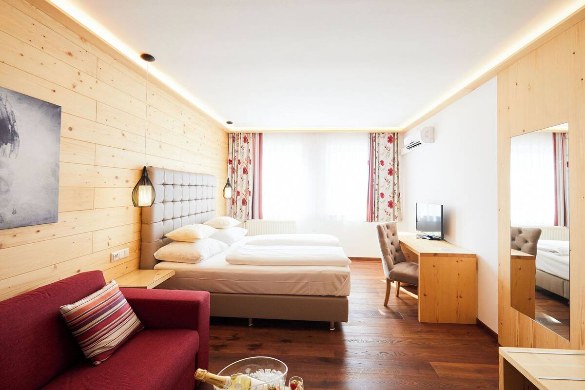 A hotel room with wooden walls, a bed, a red sofa, a TV, and a small desk.
