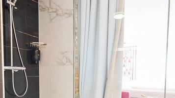 Een moderne badkamer met een douche, een glazen wand en uitzicht op een zithoek met een roze bank en een houten tafel.