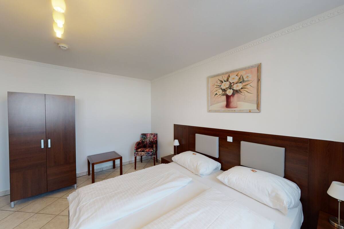 A hotel room with a large bed, a wardrobe, a small table, a chair, and a painting on the wall.