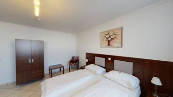 Habitación de hotel con una cama grande, un armario, una mesita, una silla y un cuadro en la pared.