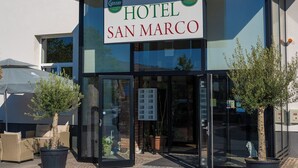 A hotel named "HOTEL SAN MARCO" with a clear entrance, potted plants, and wicker furniture outside. - Hotel San Marco (Lannach)