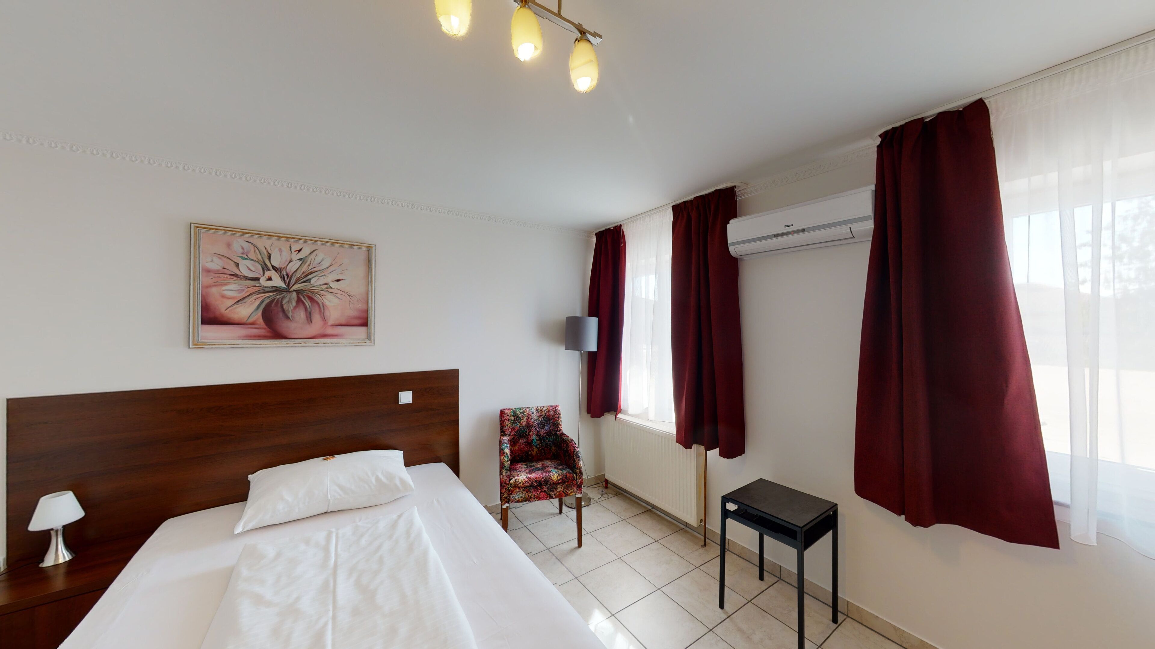 Habitación de hotel con una cama de cabecera de madera, una mesita, una silla y un cuadro en la pared.