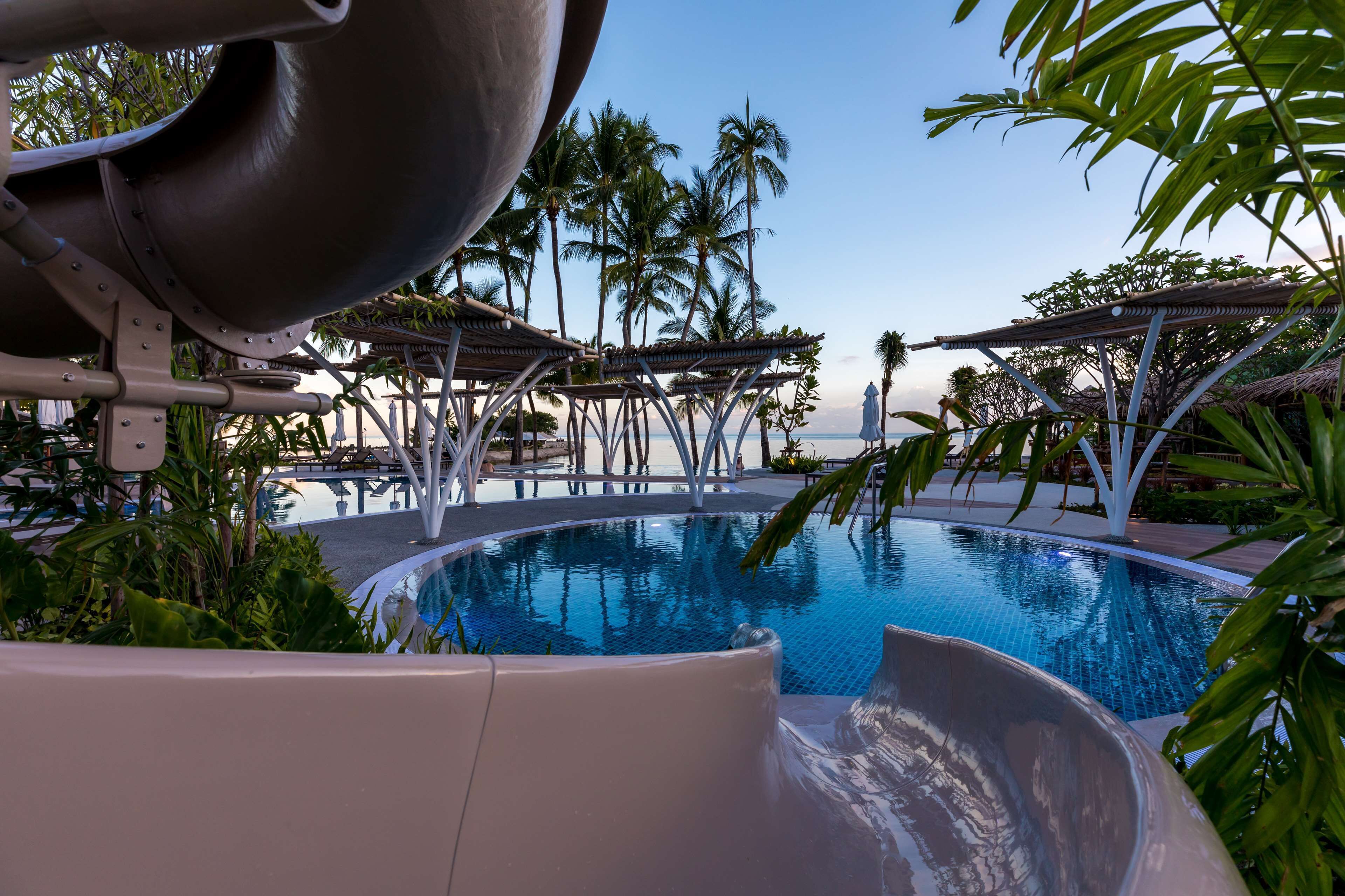 A swimming pool with a water slide, palm trees, and lounge chairs.