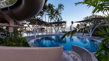 A swimming pool with a water slide, palm trees, and lounge chairs.