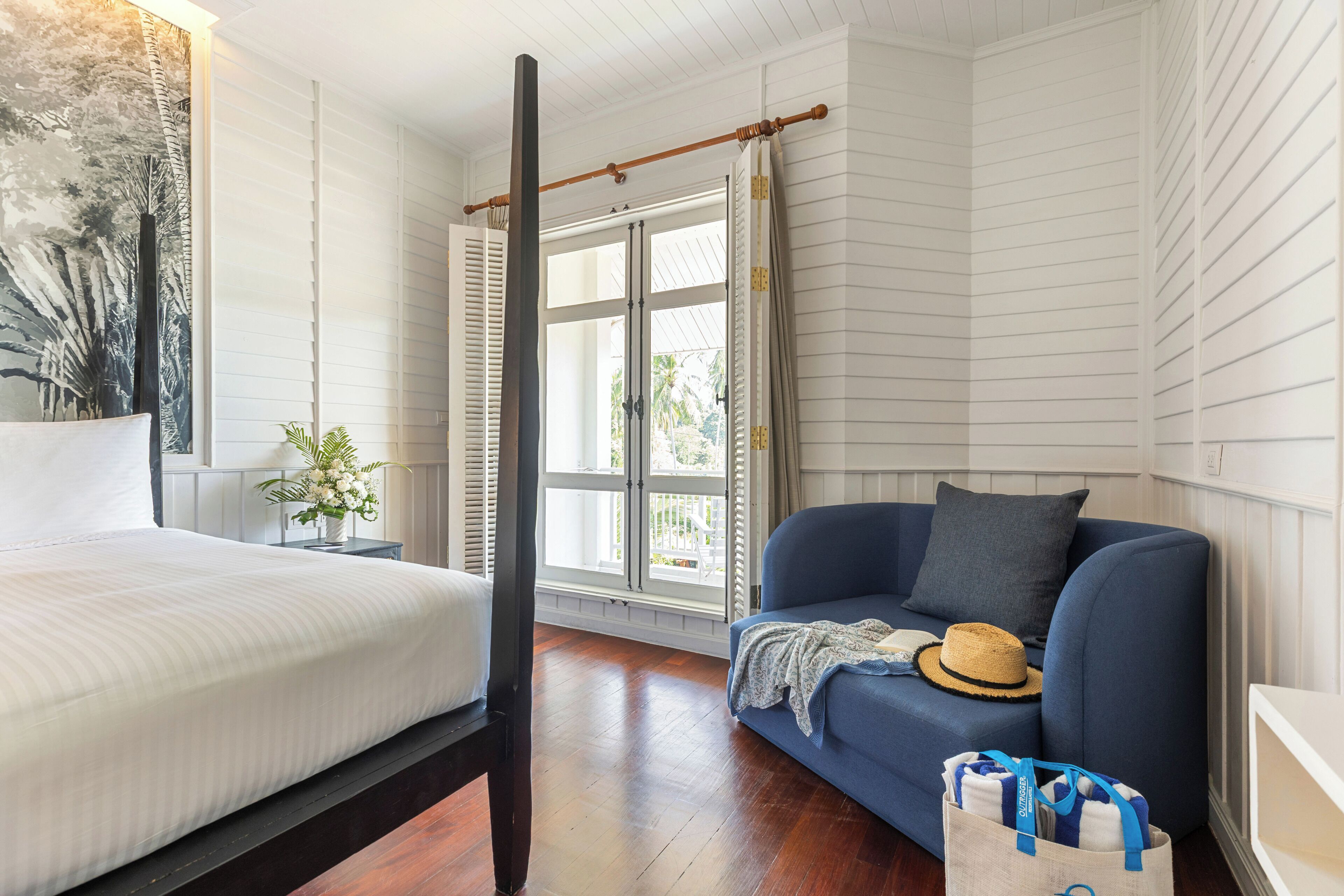 A room with a bed, a blue sofa, a window with curtains, a plant, and a wall with a vertical design.