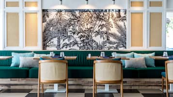 Ein Restaurant mit einem grünen Sofa, Holzstühlen und einem großen Wandgemälde.