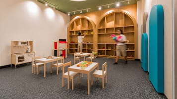 A children's playroom with tables, chairs, and shelves.