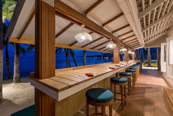 A beachside bar with wooden stools and a long counter, overlooking the ocean. - OUTRIGGER Koh Samui Beach Resort (Koh Samui)