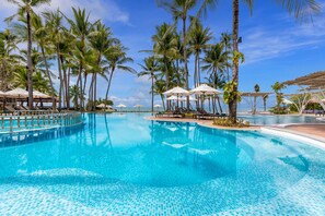 A swimming pool with palm trees, umbrellas, and lounge chairs.