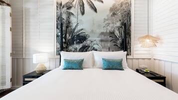 A neatly made bed with white linens and two teal pillows, a nightstand with a lamp, a phone, and a small plant.