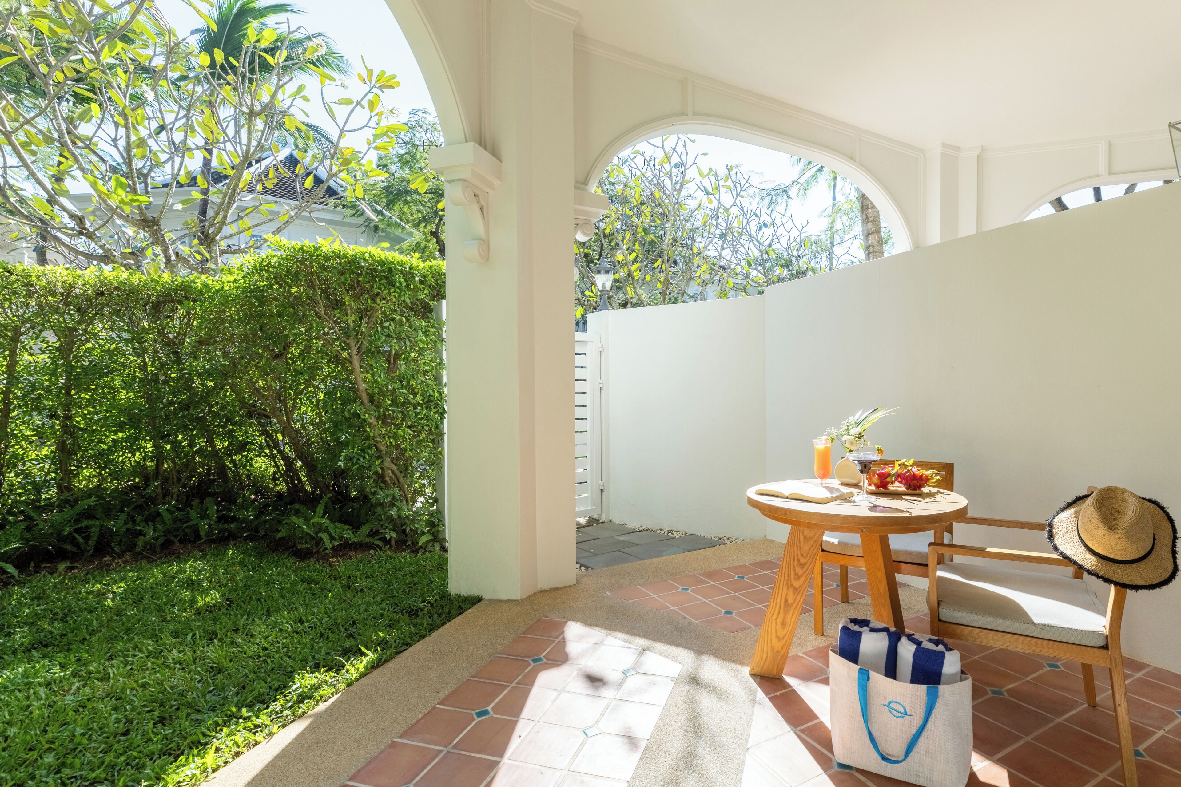 A patio with a round wooden table, a chair, a straw hat, and a bag.