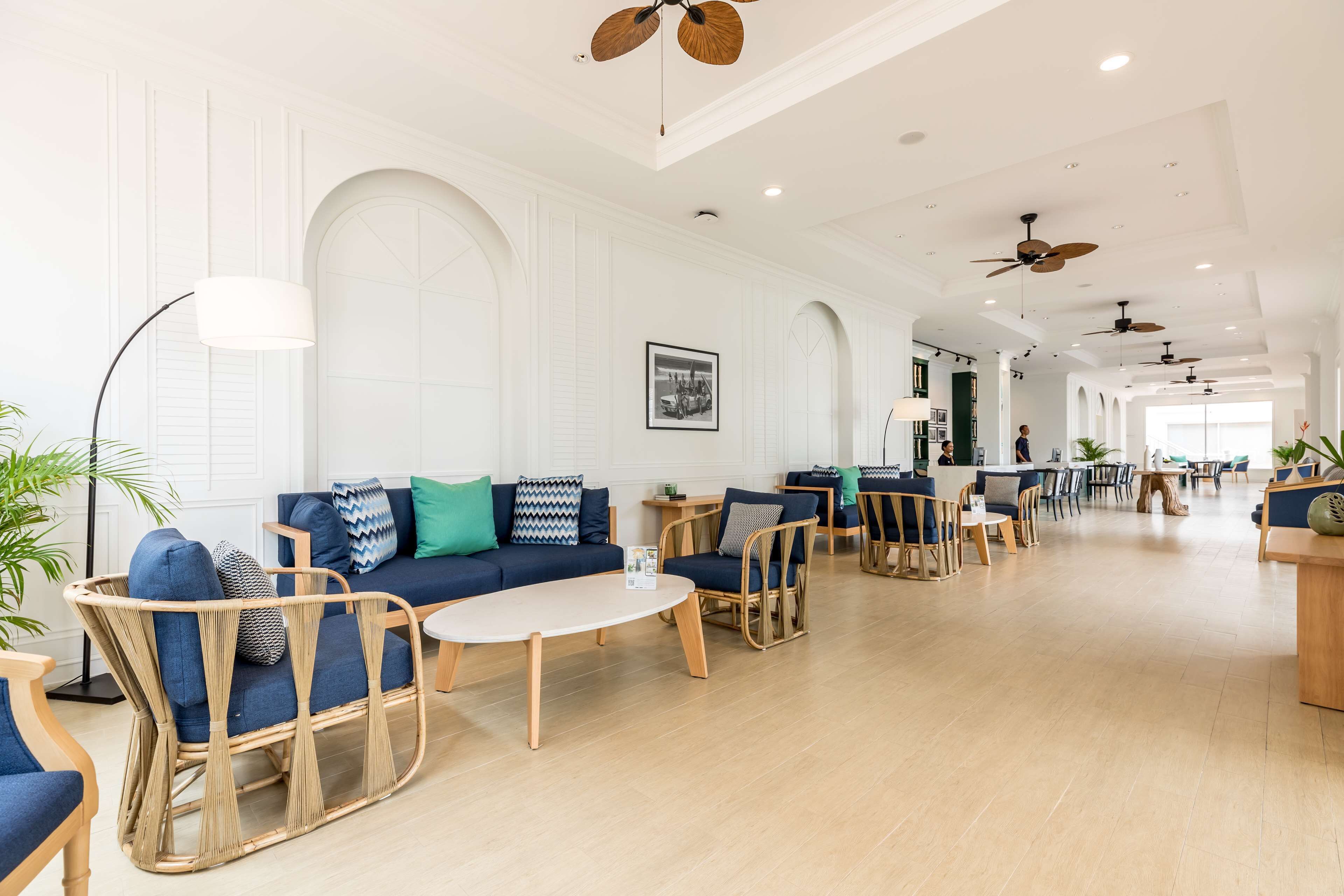 A spacious lobby with a blue sofa, wicker chairs, a coffee table, and ceiling fans.