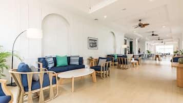 A spacious lobby with a blue sofa, wicker chairs, a coffee table, and ceiling fans.