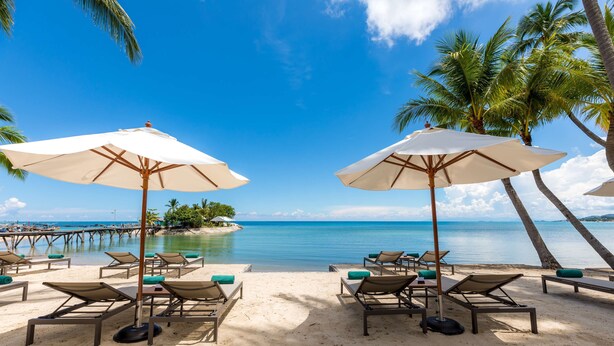 A beach with lounge chairs and umbrellas, palm trees, and a clear blue sky. - OUTRIGGER Koh Samui Beach Resort (Koh Samui)