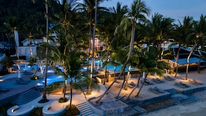 Un resort con piscina, palmeras y zonas de descanso.