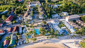 Vista aérea de un complejo turístico con varias edificaciones, una piscina y una playa.