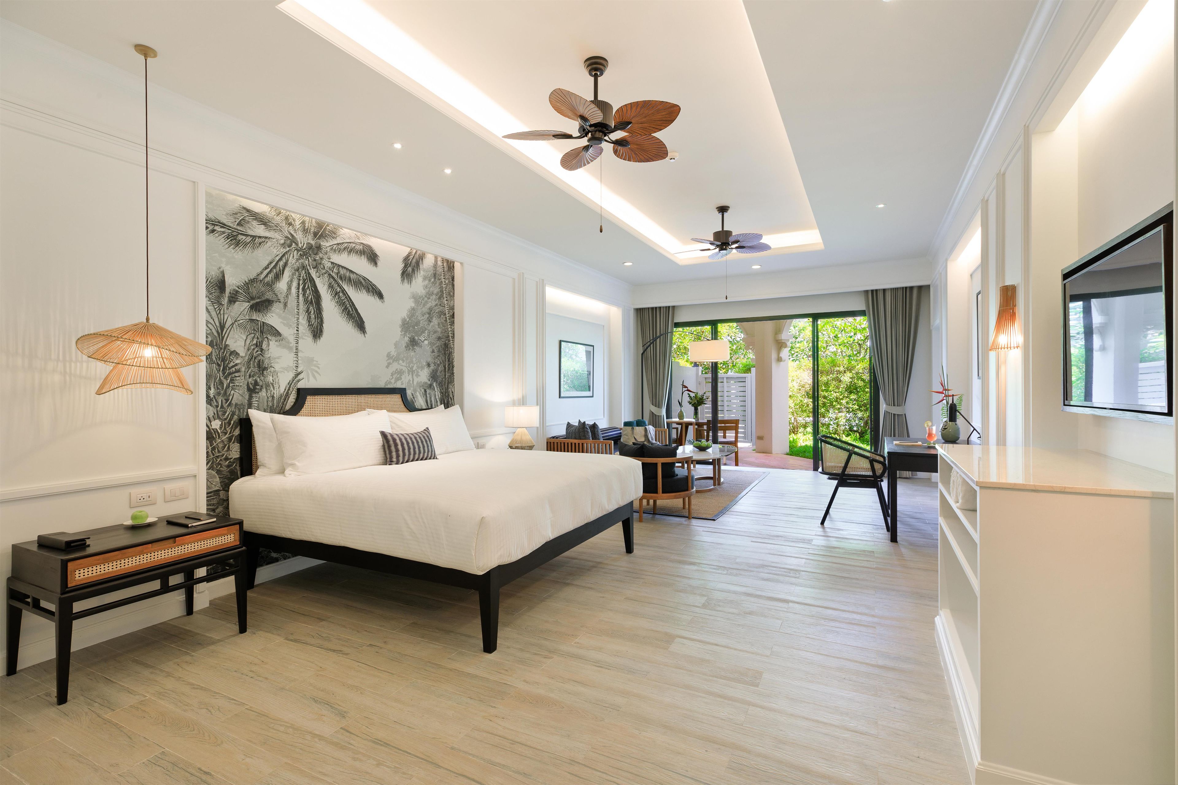 Quarto moderno com cama grande, ventilador de teto, TV na parede e vista para o exterior por uma porta deslizante.