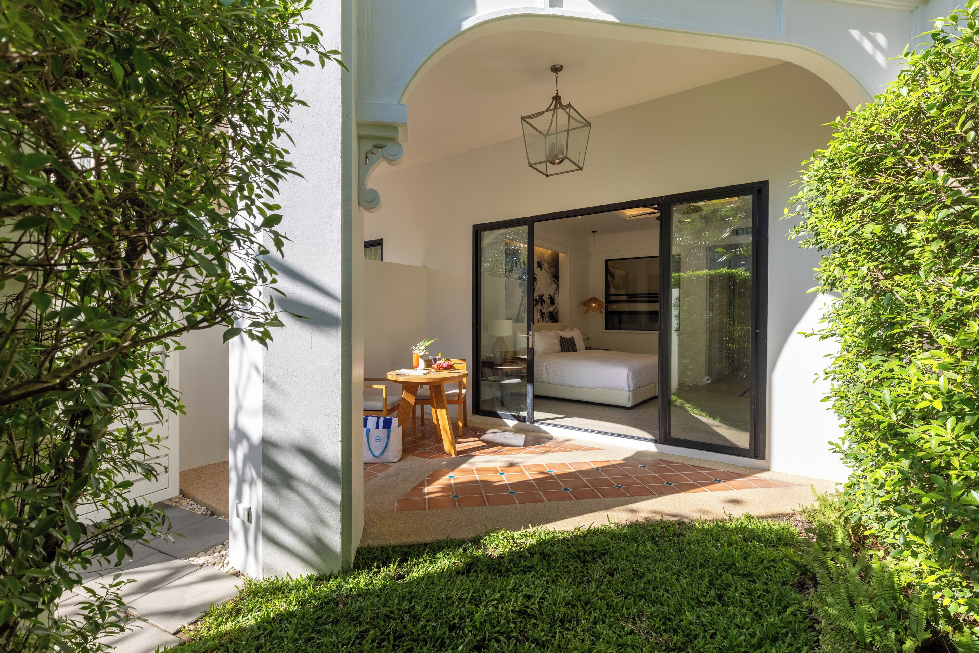 A modern building with a patio area, a dining table with chairs, and a bed visible through glass doors.