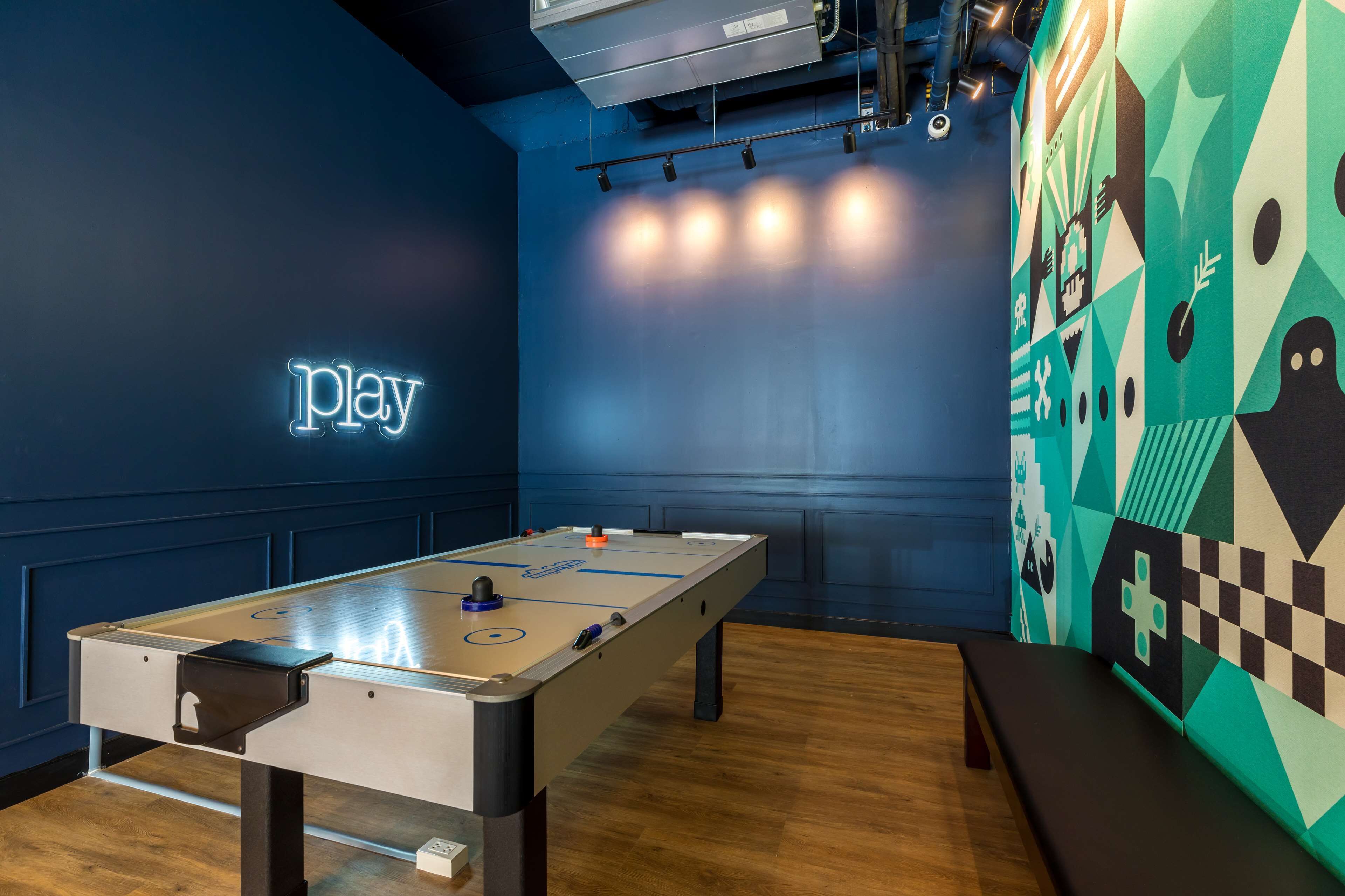 Une pièce avec une table de baby-foot, un néon et un motif géométrique sur le mur.