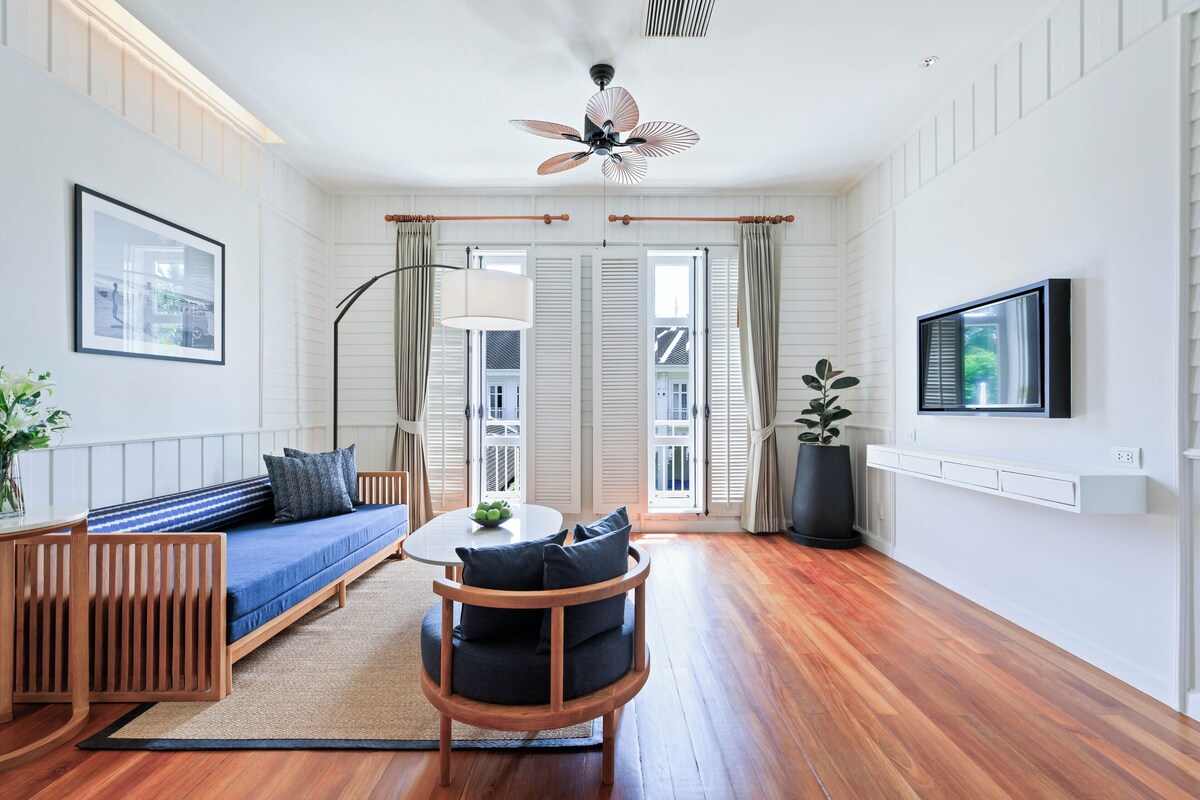 A modern living room with a sofa, a round table, a ceiling fan, and a TV mounted on the wall.