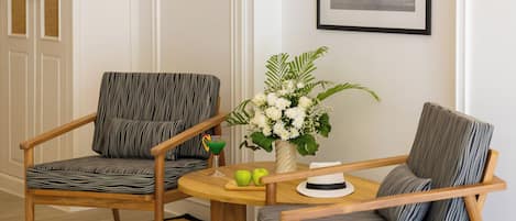 A room with two chairs, a table with a vase of flowers, and a framed picture on the wall.
