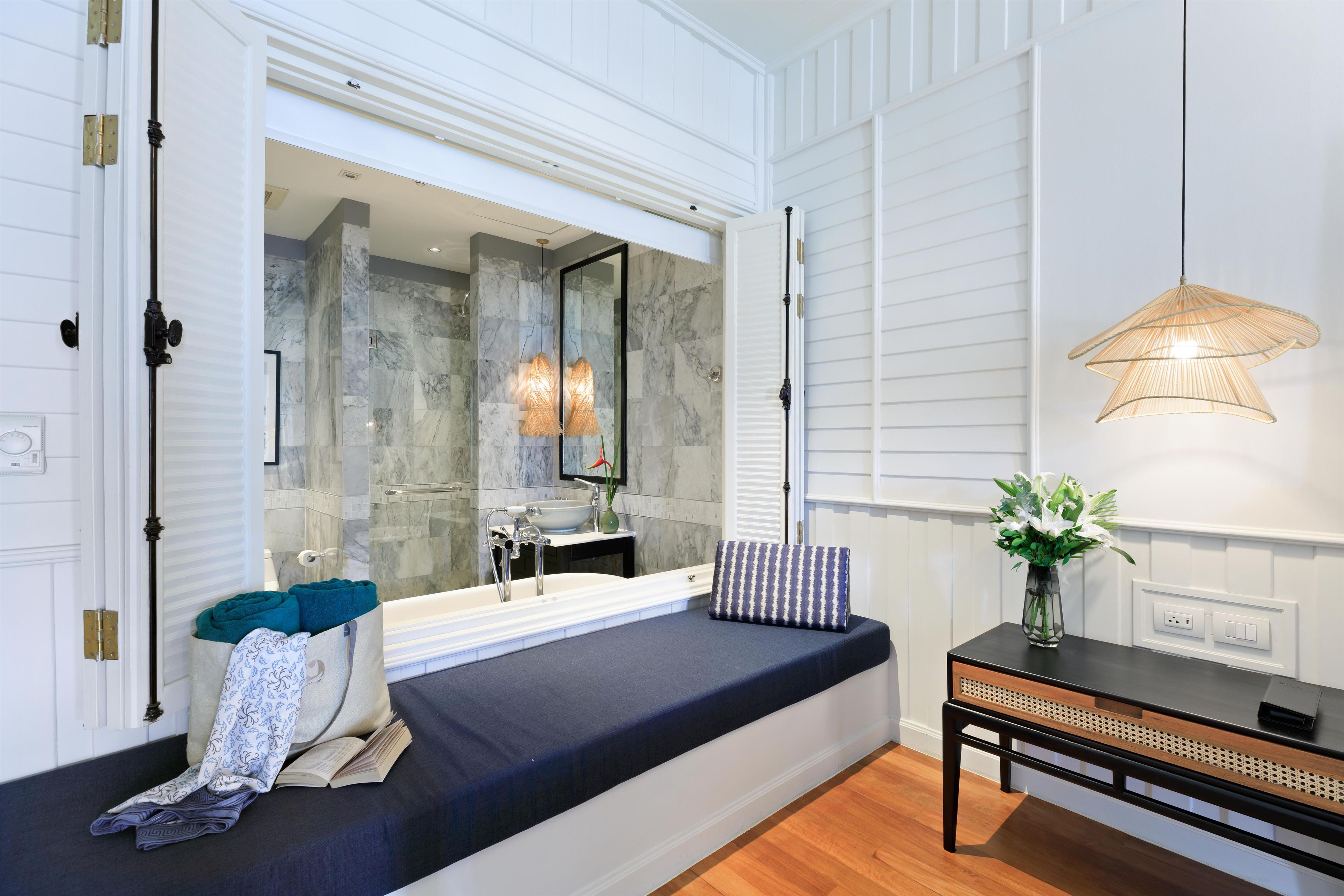 A modern bathroom with a large mirror, marble walls, a bathtub, and a window with a view.