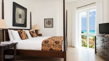 A four-poster bed with a floral bedspread, a television on a dresser, and a view of the ocean through large windows.