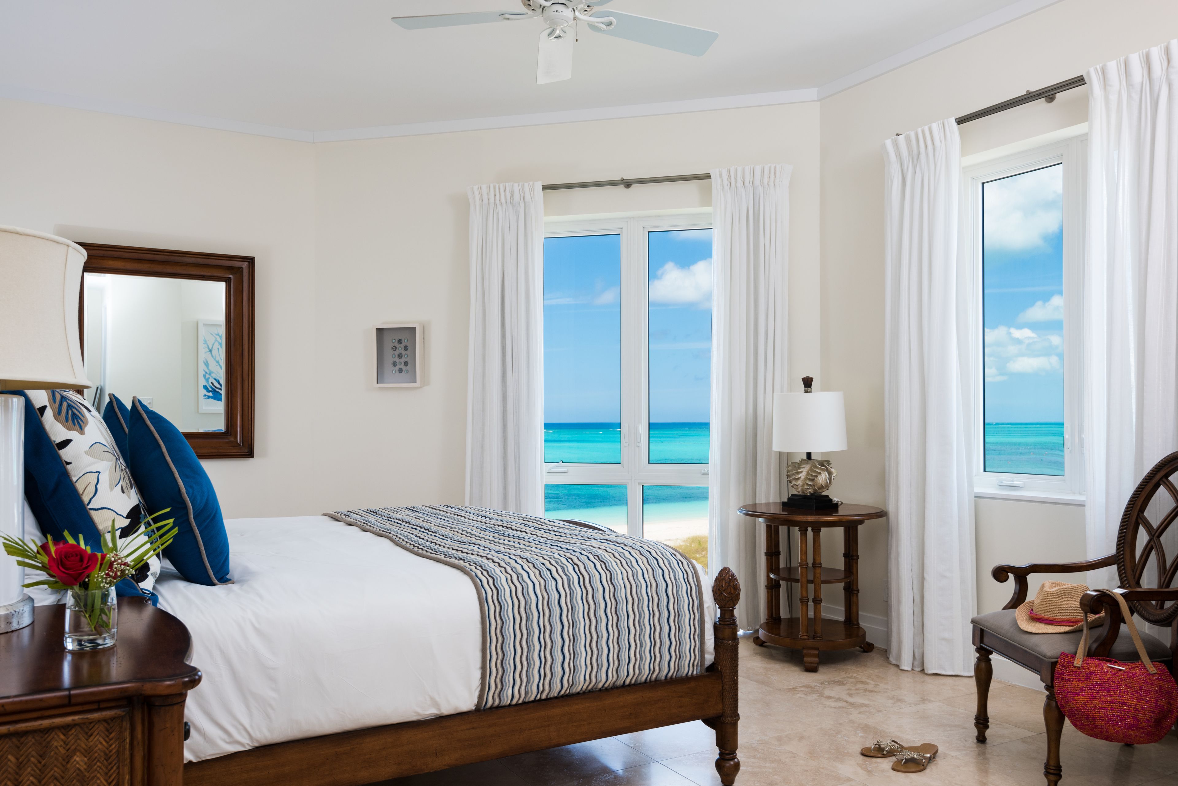A bedroom with a bed, a chair, a table, and a view of the ocean.