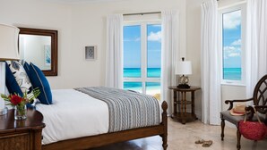 A bedroom with a bed, a chair, a table, and a view of the ocean.