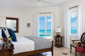 A bedroom with a bed, a chair, a table, and a view of the ocean.