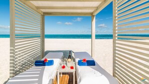 A beachside lounge with two reclining chairs, a table with a bottle and glasses, and a view of the ocean.