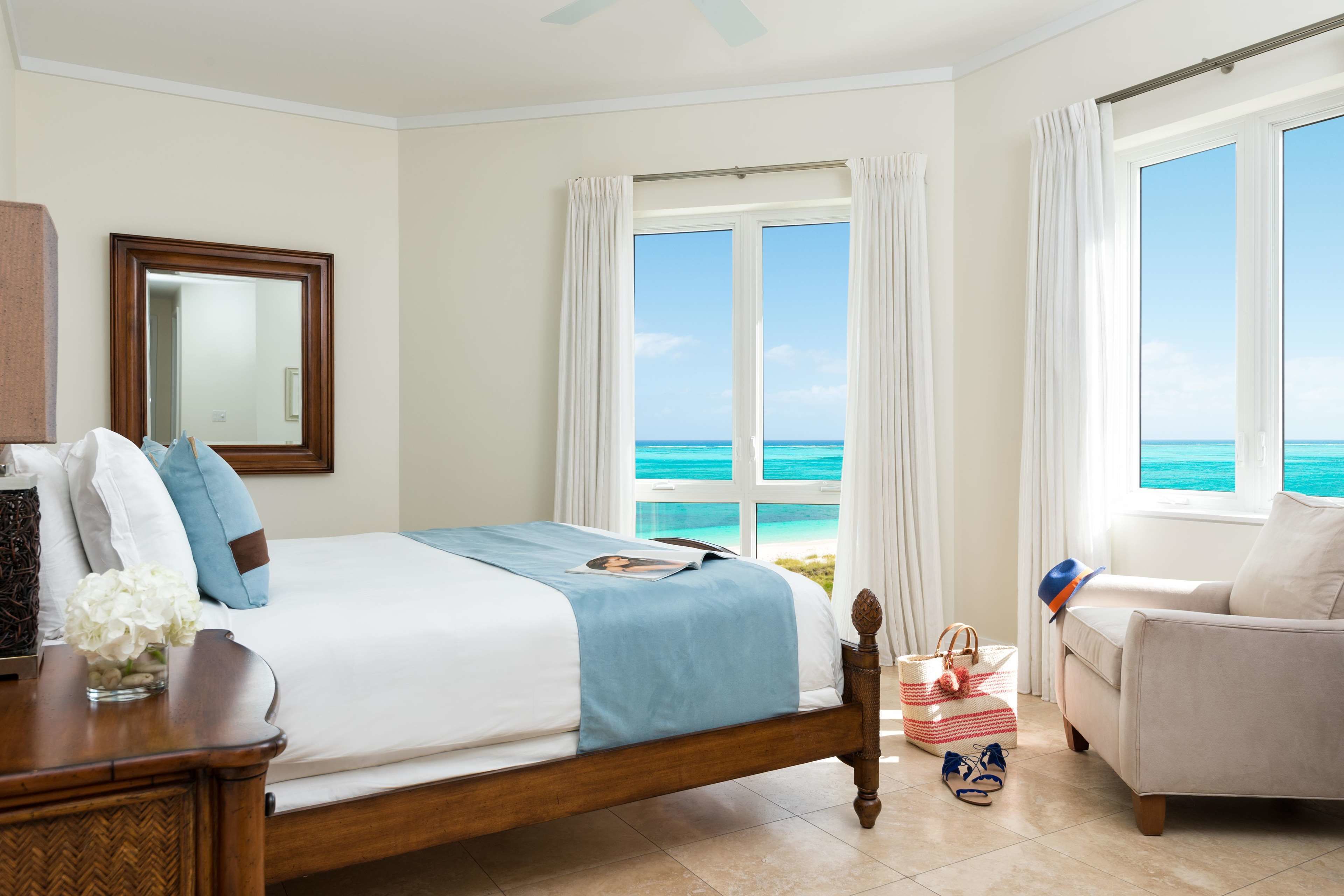 A bedroom with a bed, a nightstand, a dresser, a window with a view of the ocean, and a chair.