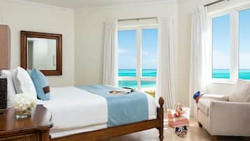 A bedroom with a bed, a nightstand, a dresser, a window with a view of the ocean, and a chair.